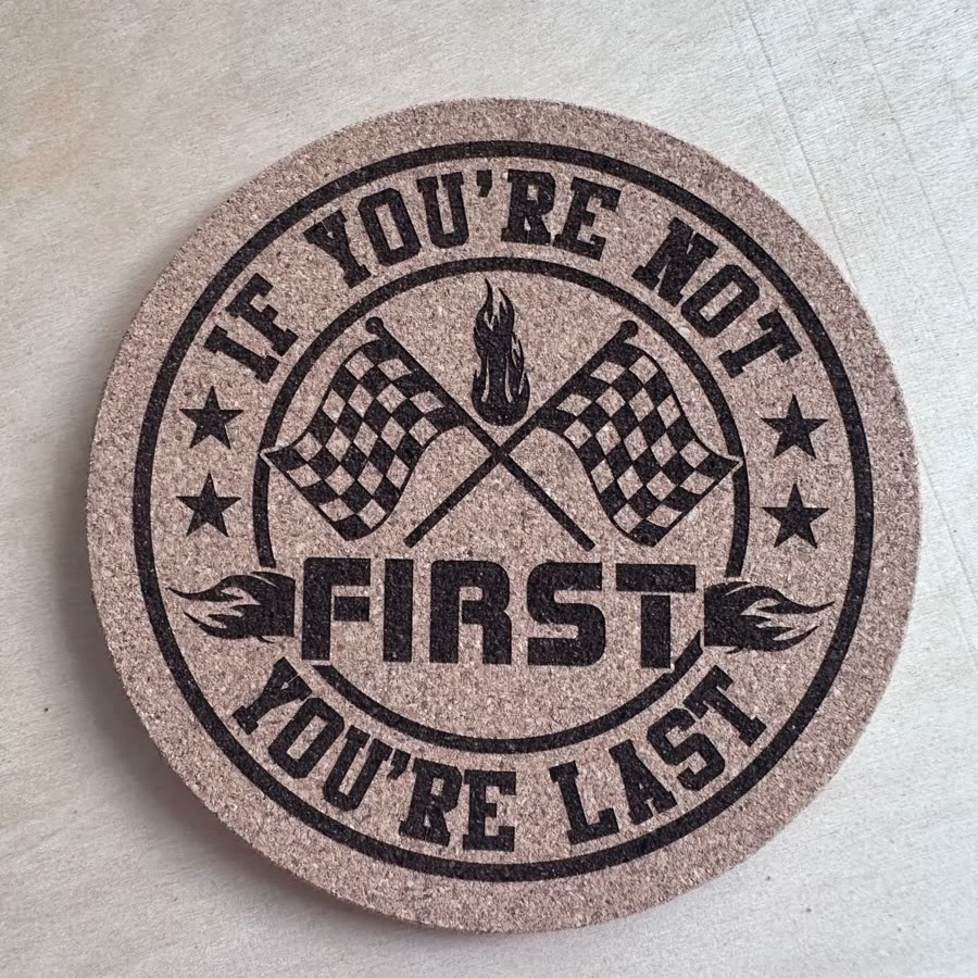 Round cork coaster engraved: If you're not first you're last, with racing flags
