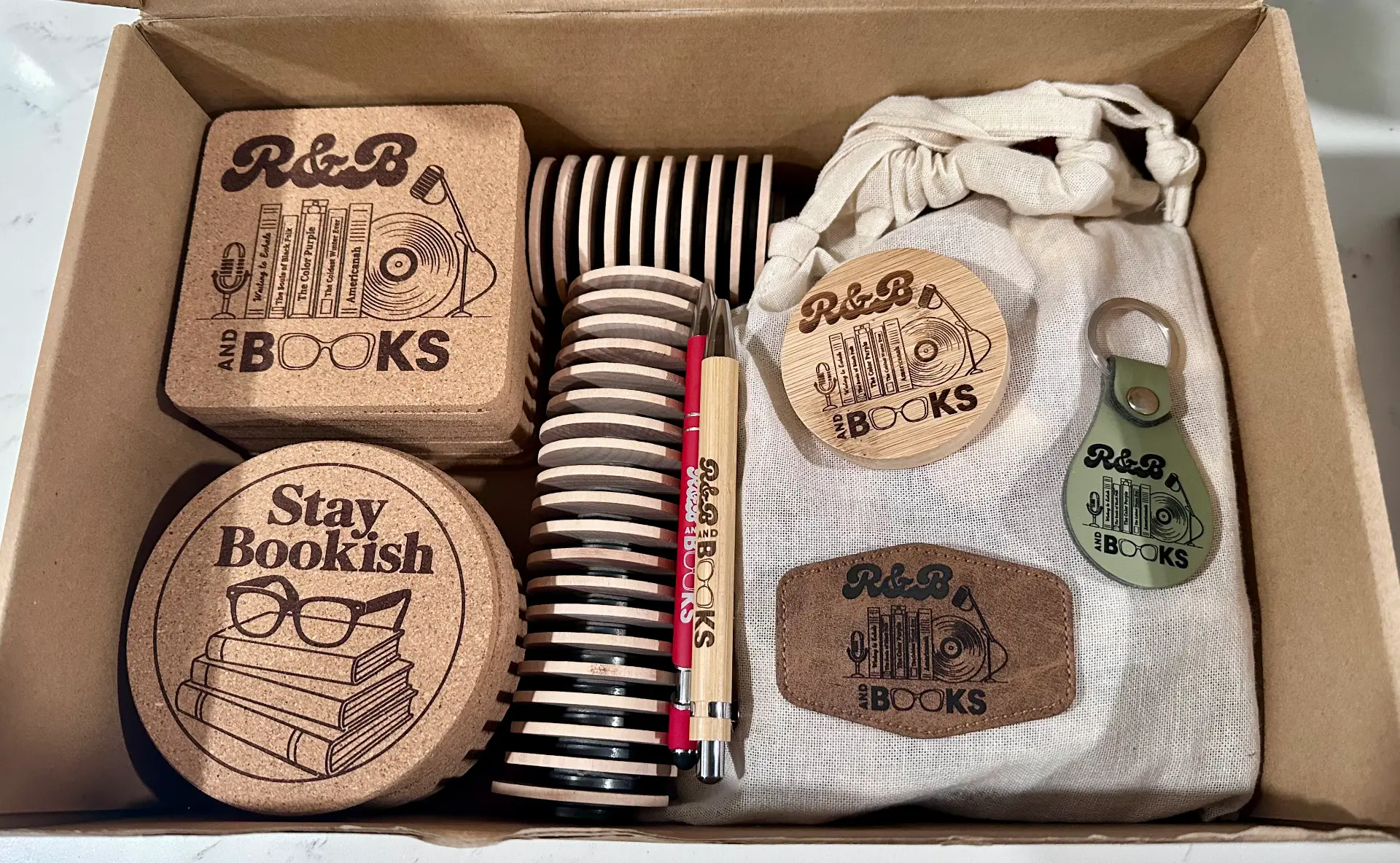 Box of branded coasters, keychains, patches, and pens for R&B and Books