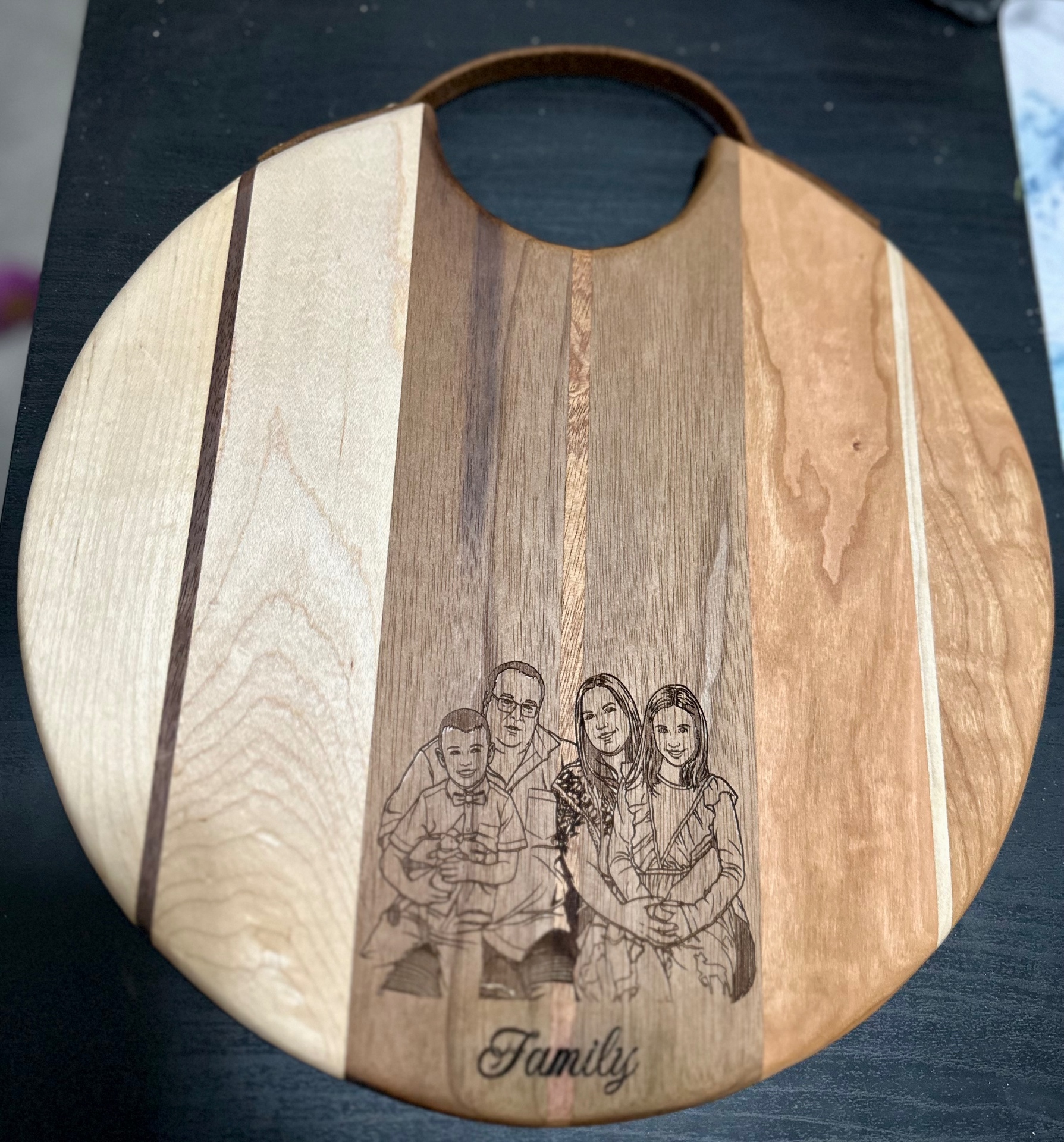 Round mixed-wood cutting board engraved with a family portrait