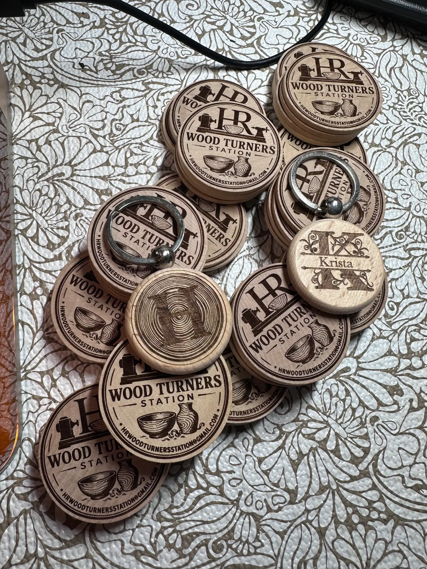 Stacks of maple round keychains and tags engraved with the Wood Turners Station logo