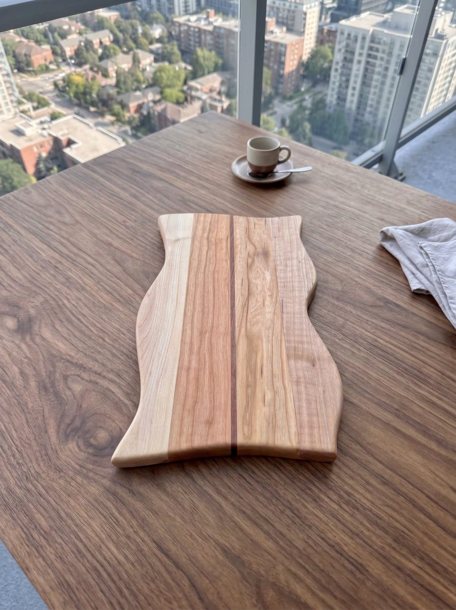Curvy edge gathering board centered on a walnut table with an espresso cup to the side